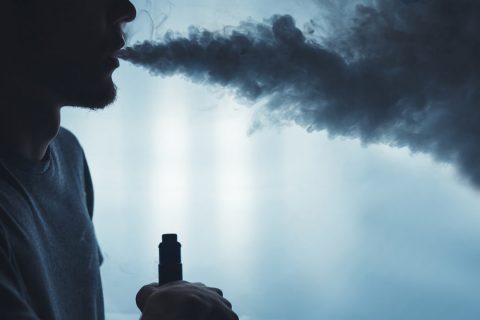 A bearded man vaping with a cloud of smoke