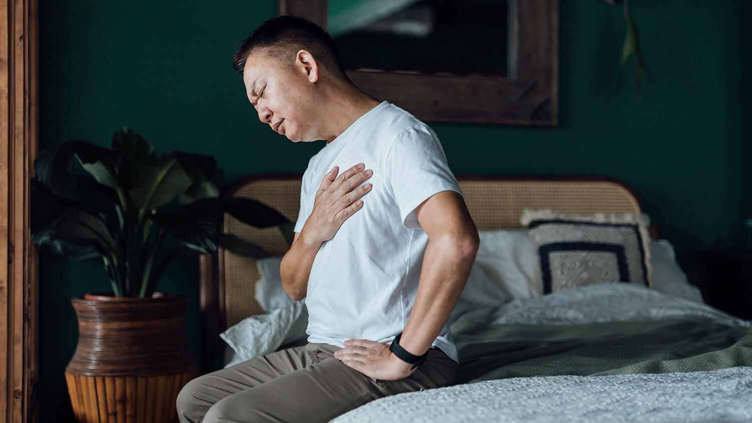 Man holding his chest in pain while sitting on a bed.