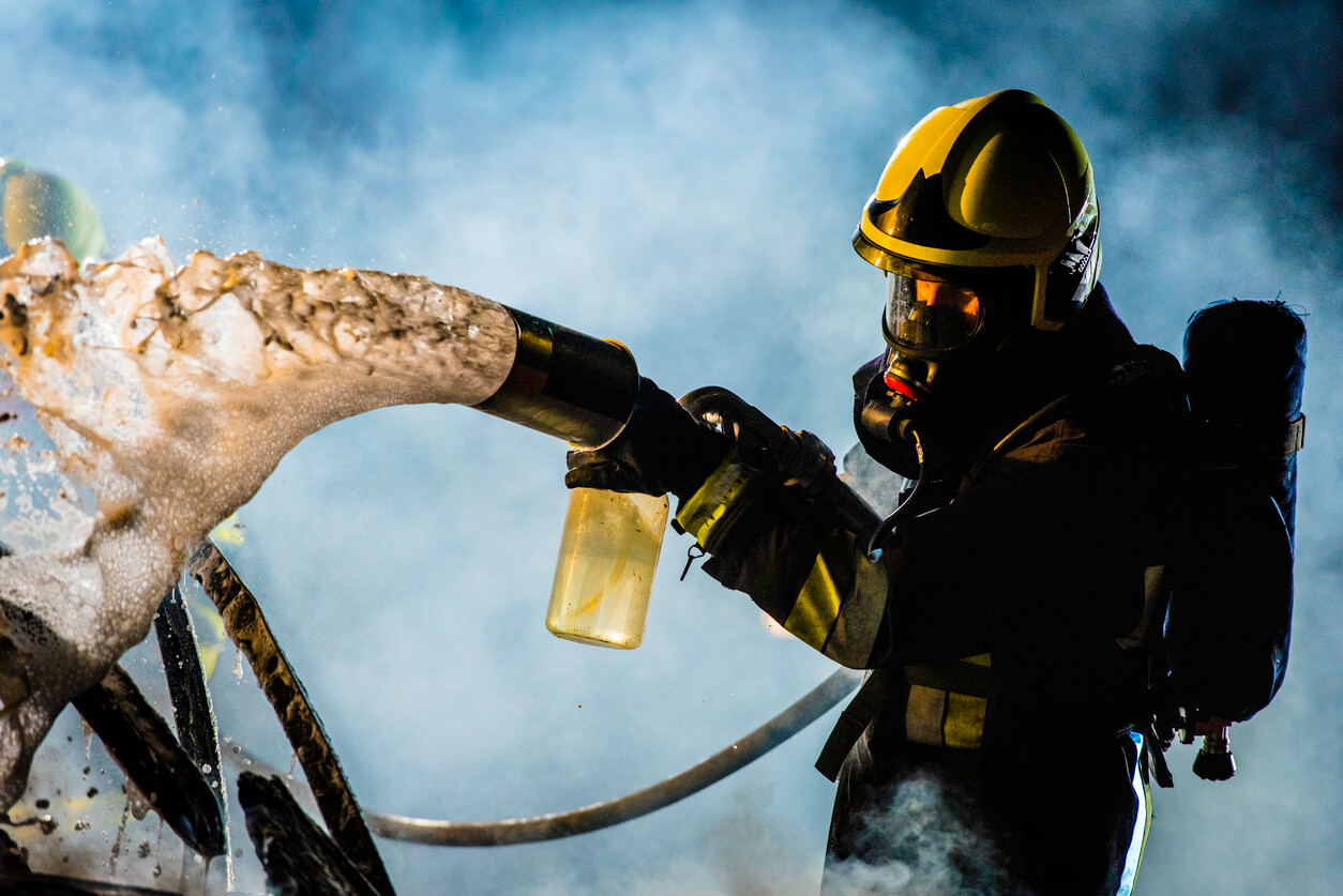 Firefighter extinguishing car fire with foam spray