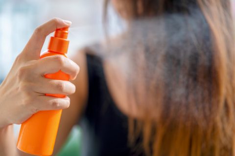 Young woman applying hair spray in bathroom