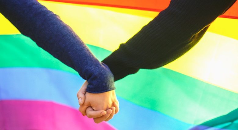 Couple holding hands in front of the Pride flag