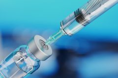 Medical disposable syringe for vaccine injection and glass vial on blue blur background.