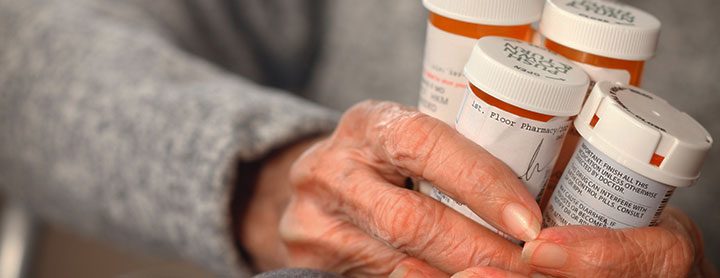 older woman holding a variety of prescription bottles